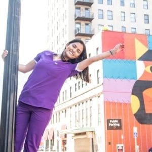 Woman in purple scrubbs hanging from a lamp post