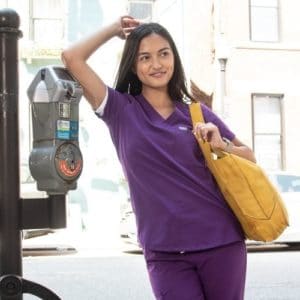 Woman in purple scrubs leaning on a parking meter.